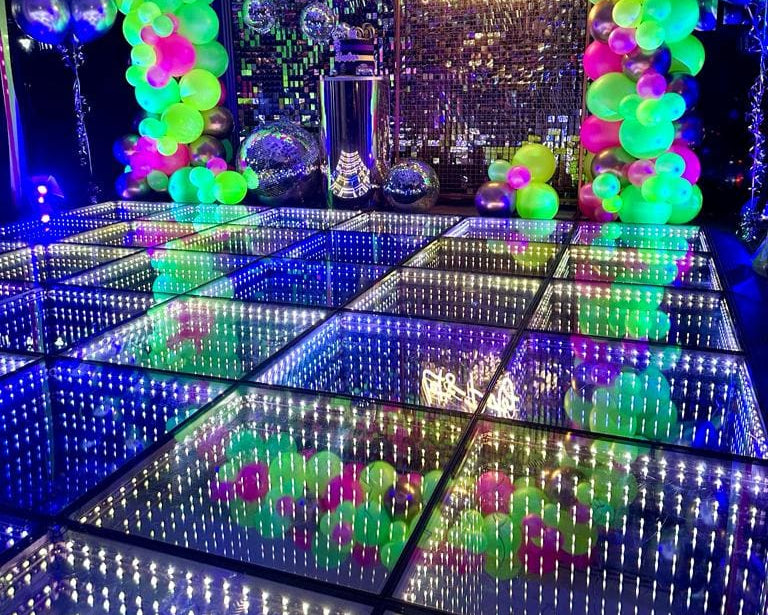 Decorated room with colorful balloons, LED floor, and disco ball.